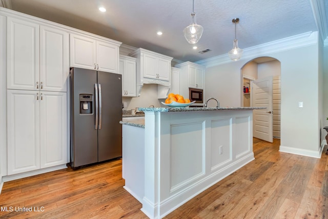 kitchen featuring hanging light fixtures, black microwave, an island with sink, white cabinets, and stainless steel fridge with ice dispenser