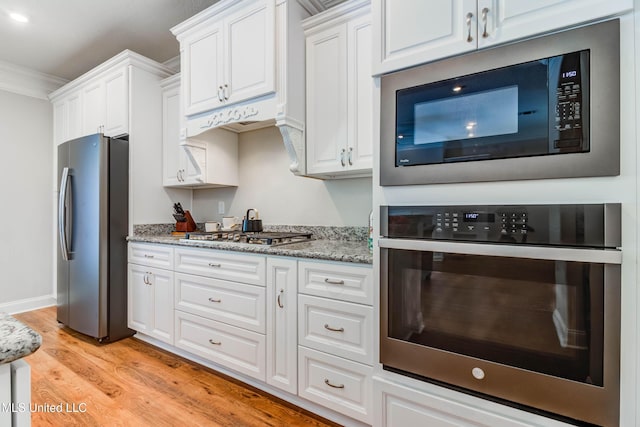 kitchen with appliances with stainless steel finishes, white cabinets, crown molding, light stone countertops, and light hardwood / wood-style flooring