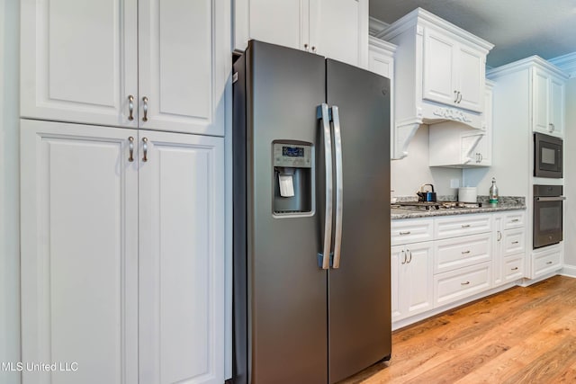 kitchen featuring crown molding, light stone countertops, black appliances, white cabinets, and light wood-type flooring