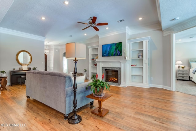 living room with crown molding, a premium fireplace, built in shelves, a textured ceiling, and light hardwood / wood-style flooring