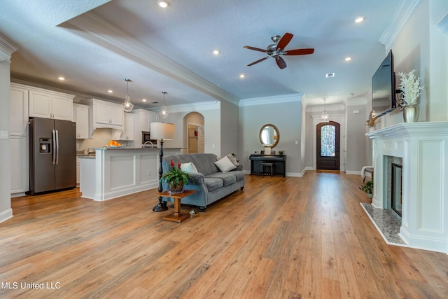 living room with ornamental molding, ceiling fan, a premium fireplace, a textured ceiling, and light hardwood / wood-style flooring