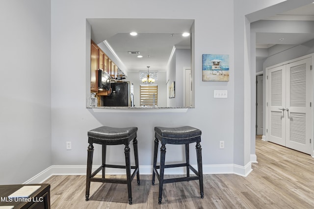 bar with stainless steel refrigerator, light stone countertops, a chandelier, and ornamental molding