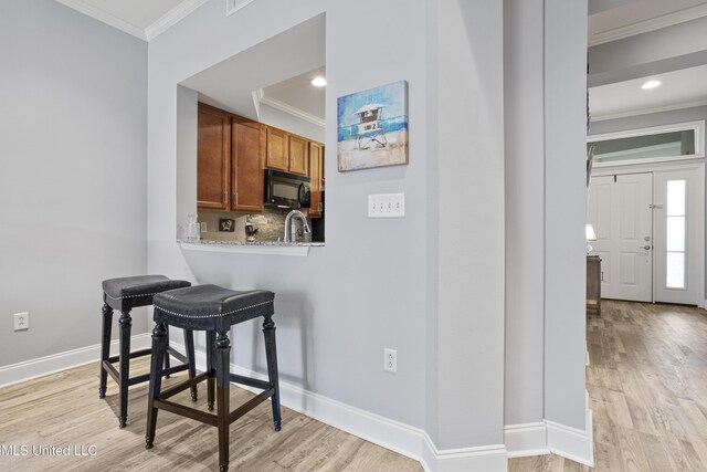 kitchen with decorative backsplash, crown molding, light stone countertops, and light hardwood / wood-style flooring