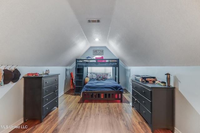 bedroom featuring visible vents, a textured ceiling, baseboards, light wood-style floors, and lofted ceiling