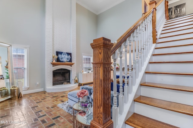 stairs featuring a high ceiling, a fireplace, crown molding, brick floor, and baseboards