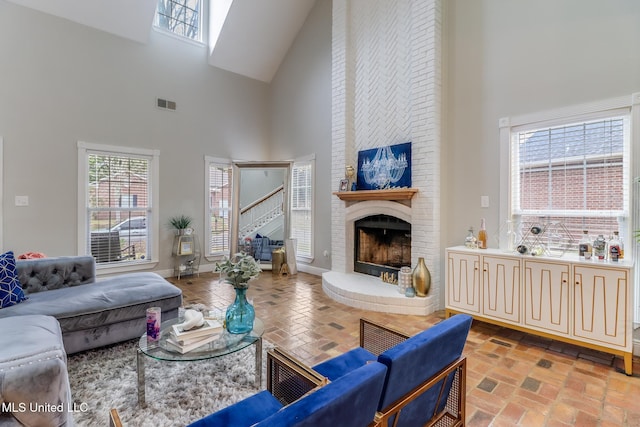 living room featuring visible vents, baseboards, a high ceiling, a fireplace, and brick floor