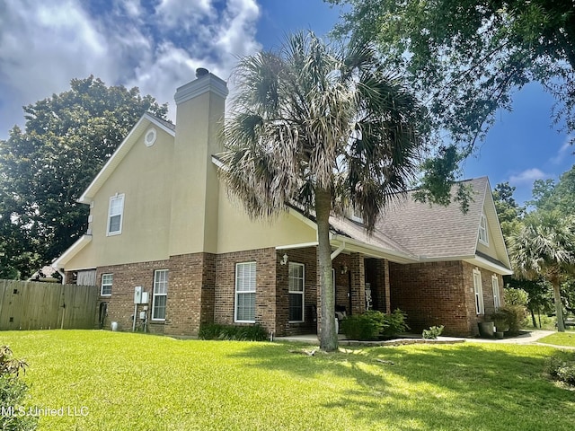 view of property exterior with fence, a chimney, stucco siding, a lawn, and brick siding