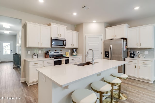 87139 Highpoint Dr, Diamondhead, MS 39525 - kitchen featuring appliances with stainless steel finishes, backsplash, a kitchen breakfast bar, a center island with sink, and white cabinets