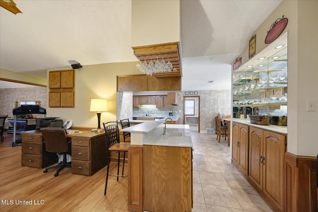 kitchen featuring sink, a textured ceiling, a kitchen bar, a kitchen island with sink, and light wood-type flooring