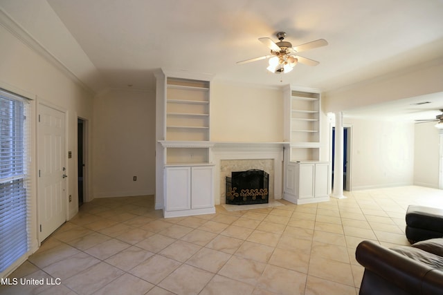 living room with built in shelves, crown molding, light tile patterned floors, ceiling fan, and a fireplace