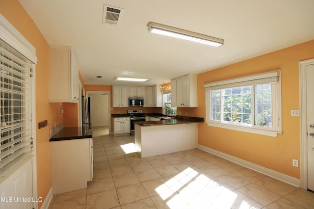 kitchen with light tile patterned flooring, sink, kitchen peninsula, stainless steel appliances, and white cabinets