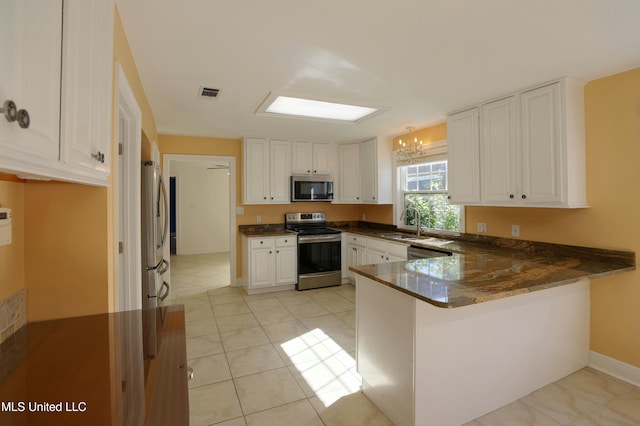 kitchen featuring white cabinetry, an inviting chandelier, appliances with stainless steel finishes, kitchen peninsula, and dark stone counters