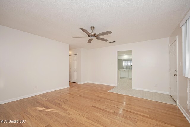 spare room featuring visible vents, a ceiling fan, a textured ceiling, light wood-type flooring, and baseboards