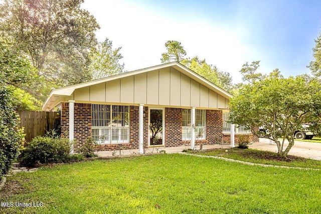 view of front of house featuring fence, a front lawn, board and batten siding, and brick siding