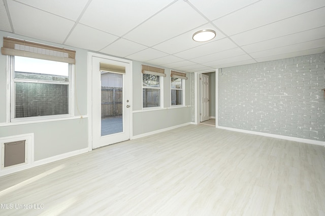 spare room with brick wall, wood finished floors, a paneled ceiling, and baseboards