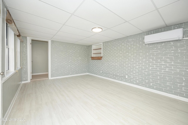 finished basement with brick wall, a drop ceiling, wood finished floors, and a wall mounted air conditioner