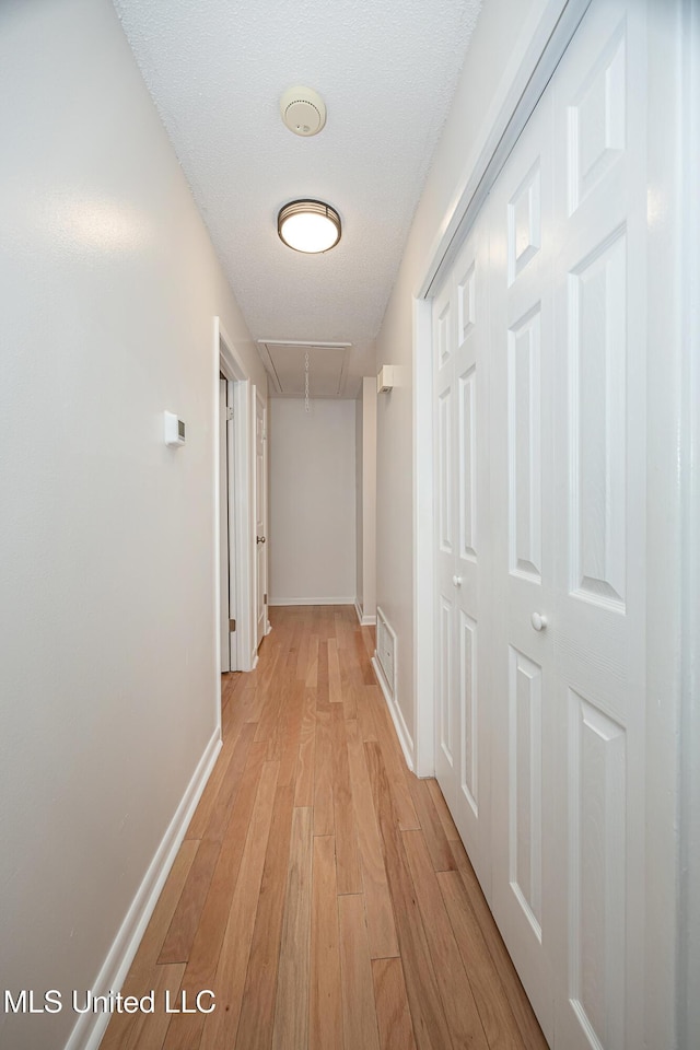 corridor with attic access, light wood-type flooring, visible vents, and baseboards