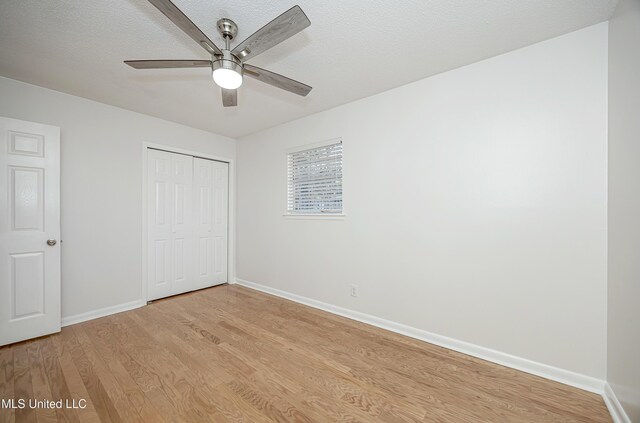 unfurnished bedroom with light wood finished floors, a textured ceiling, baseboards, and a closet