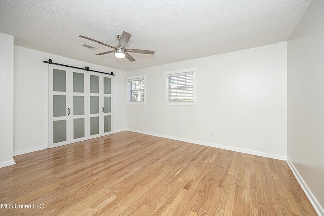 unfurnished room featuring a barn door, baseboards, visible vents, light wood-style flooring, and a textured ceiling