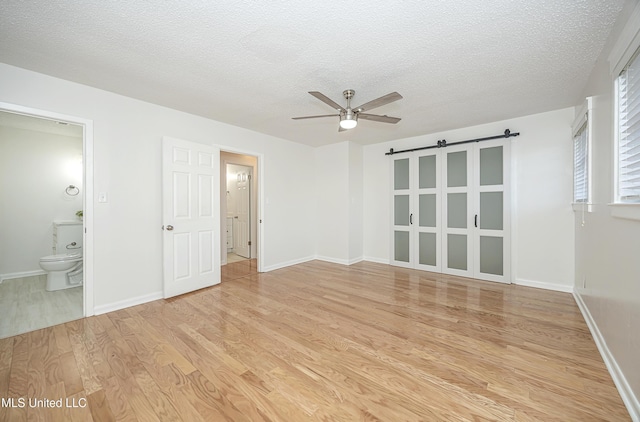 spare room with a textured ceiling, a barn door, a ceiling fan, baseboards, and light wood finished floors