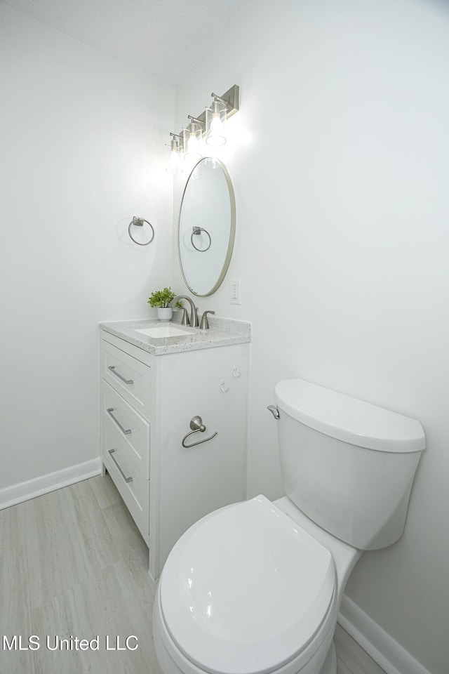 half bathroom featuring wood finished floors, vanity, toilet, and baseboards