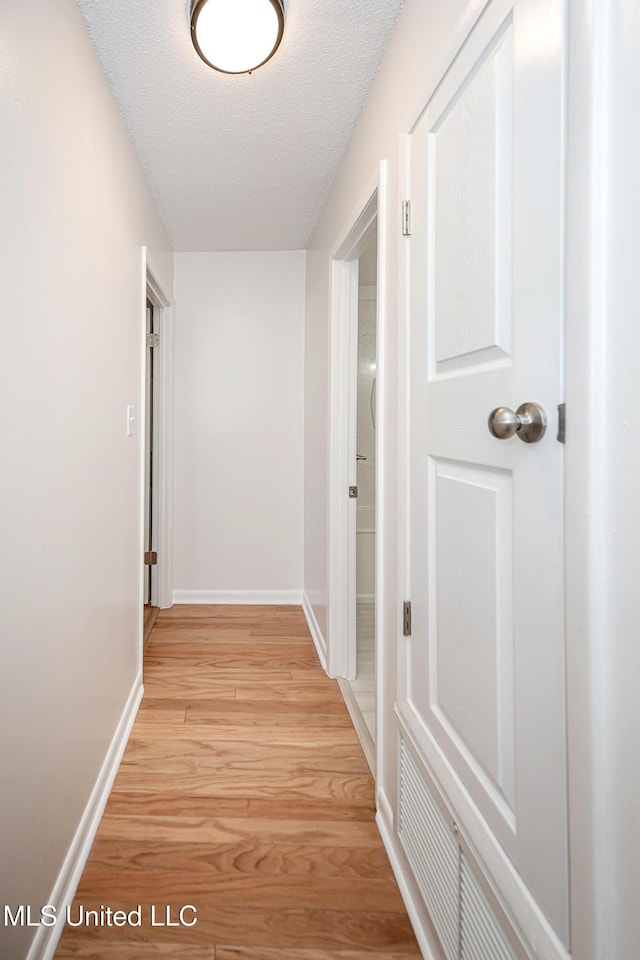 hallway featuring baseboards, a textured ceiling, and light wood finished floors