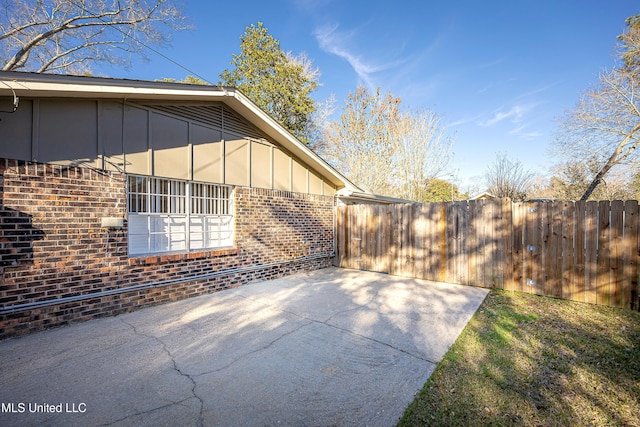 view of side of property with brick siding, board and batten siding, a patio area, and fence