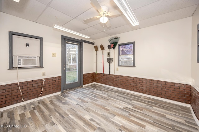 unfurnished room with cooling unit, a paneled ceiling, brick wall, and wood finished floors