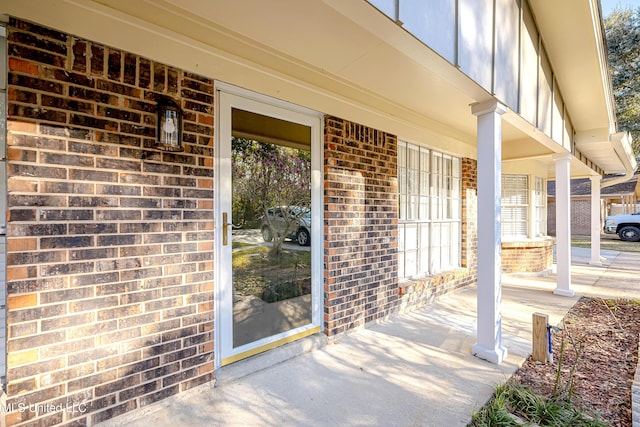 doorway to property with a porch and brick siding