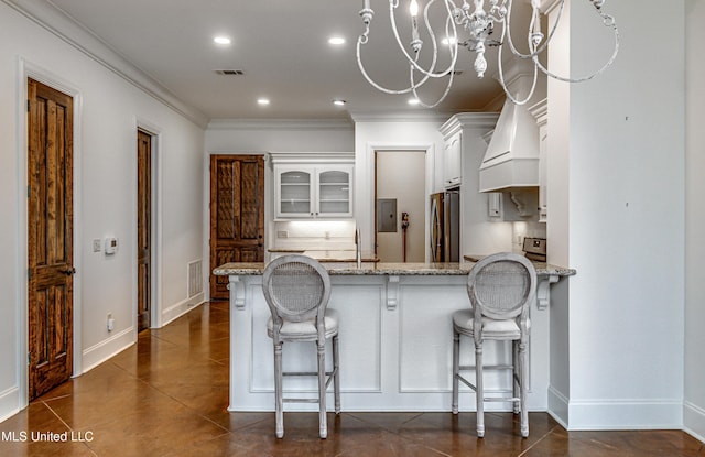 kitchen with premium range hood, a kitchen bar, stainless steel refrigerator, white cabinetry, and light stone counters