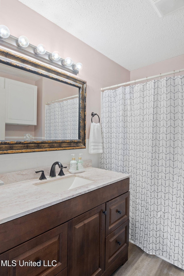 full bathroom with a textured ceiling, wood finished floors, and vanity