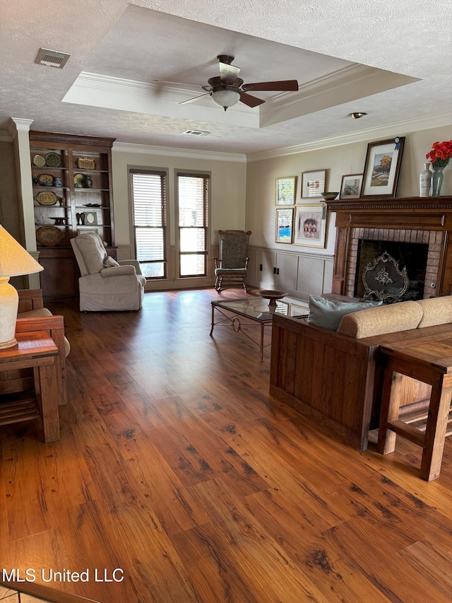 living area with crown molding, a raised ceiling, wood finished floors, and visible vents