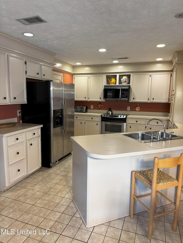 kitchen with visible vents, a peninsula, a textured ceiling, a sink, and stainless steel appliances