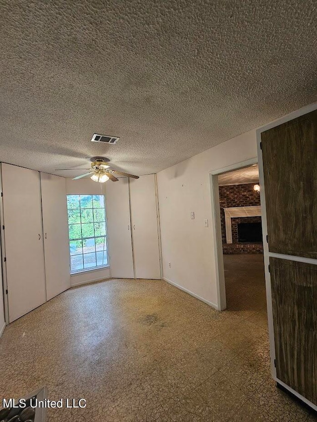 unfurnished room featuring a textured ceiling, a fireplace, and ceiling fan