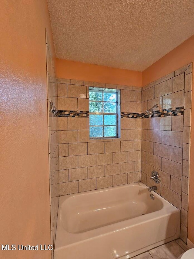 bathroom with a textured ceiling and tiled shower / bath combo