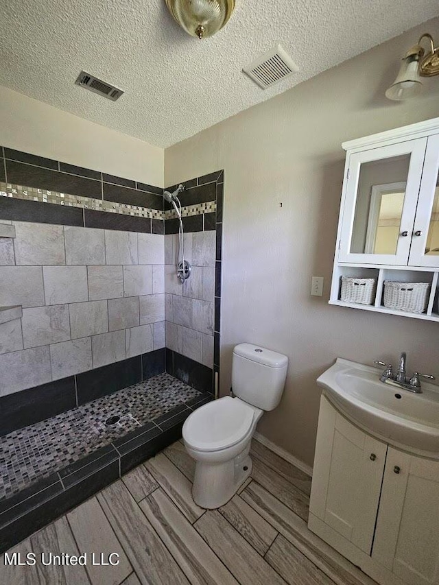 bathroom featuring vanity, toilet, a textured ceiling, and a tile shower