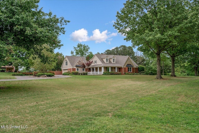 new england style home with a porch, an attached garage, driveway, and a front yard