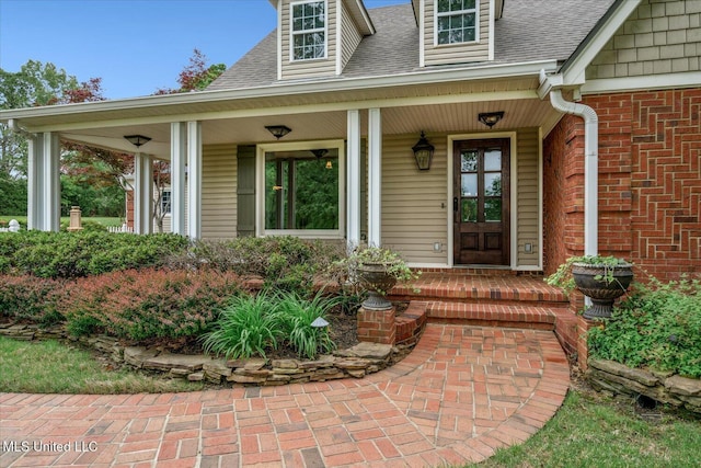 entrance to property with covered porch, brick siding, and roof with shingles