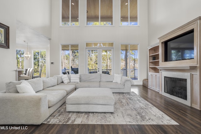 living room featuring dark wood-type flooring, french doors, a towering ceiling, and a chandelier