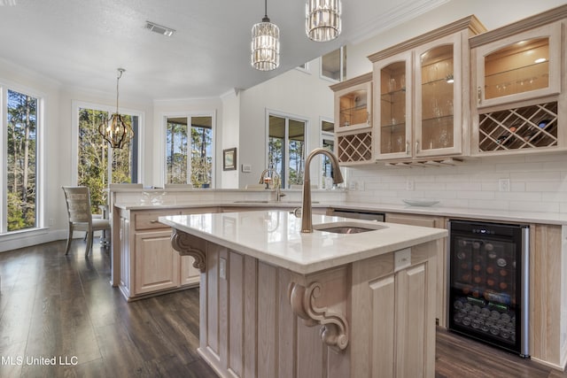 kitchen featuring hanging light fixtures, light brown cabinets, an island with sink, and beverage cooler