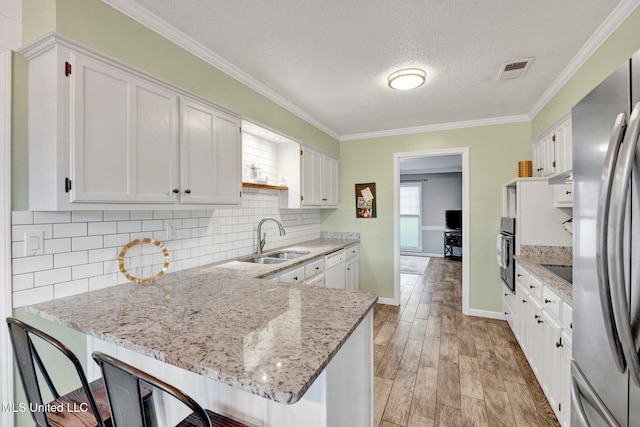 kitchen with sink, kitchen peninsula, appliances with stainless steel finishes, white cabinets, and light wood-type flooring