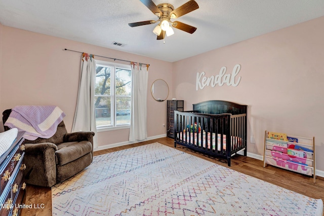 bedroom with ceiling fan, a nursery area, a textured ceiling, and wood-type flooring