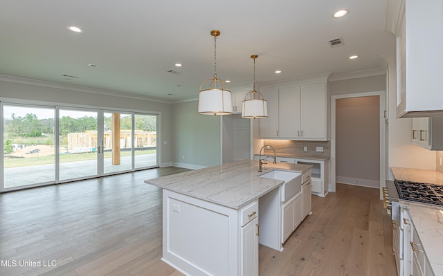 kitchen with white cabinetry, light hardwood / wood-style flooring, decorative light fixtures, and an island with sink