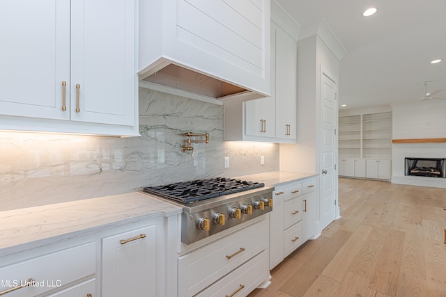 kitchen featuring stainless steel gas stovetop, decorative backsplash, white cabinetry, a fireplace, and light wood-type flooring