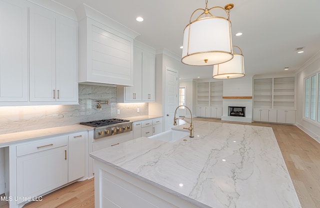 kitchen featuring light wood-type flooring, white cabinetry, hanging light fixtures, sink, and stainless steel gas cooktop