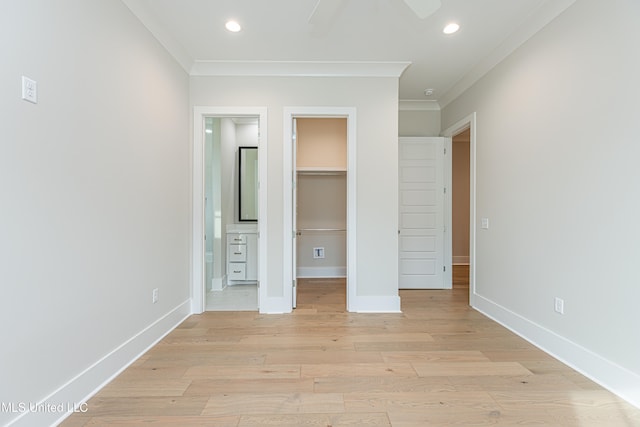 unfurnished bedroom featuring light wood-type flooring, a spacious closet, ceiling fan, and crown molding