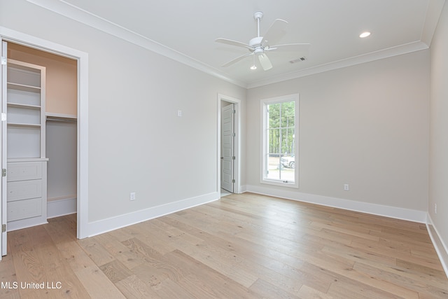 unfurnished bedroom with a closet, a walk in closet, crown molding, light hardwood / wood-style floors, and ceiling fan