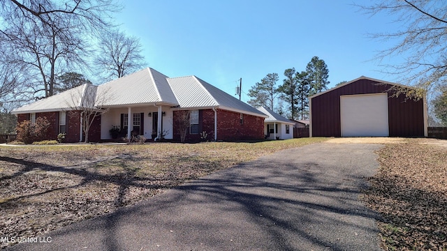 view of front of property with metal roof, covered porch, brick siding, an outdoor structure, and driveway