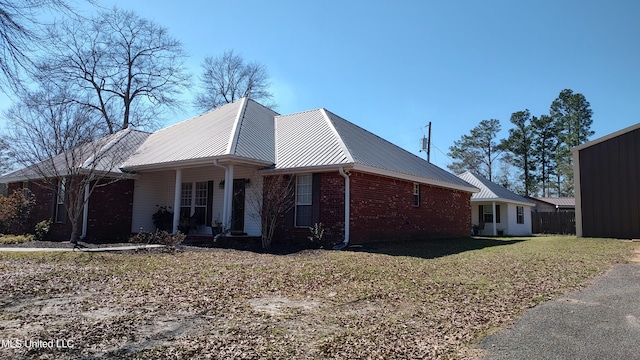 view of property exterior with a porch, brick siding, metal roof, and a lawn