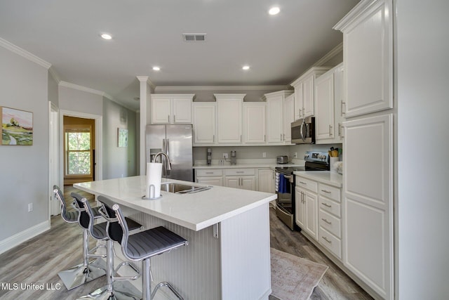 183 Mcdonnell Ave Unit 305, Biloxi, MS 39531 - kitchen featuring stainless steel appliances, light wood finished floors, white cabinets, a kitchen island with sink, and crown molding